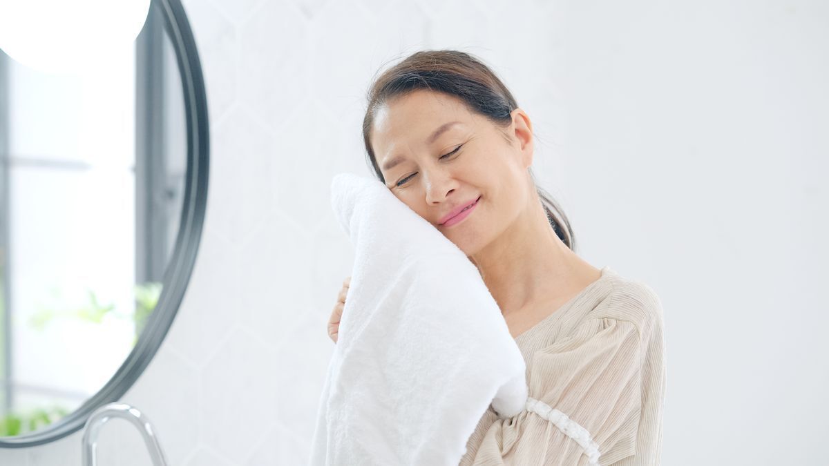 Older Asian woman patting her face with a white towel.