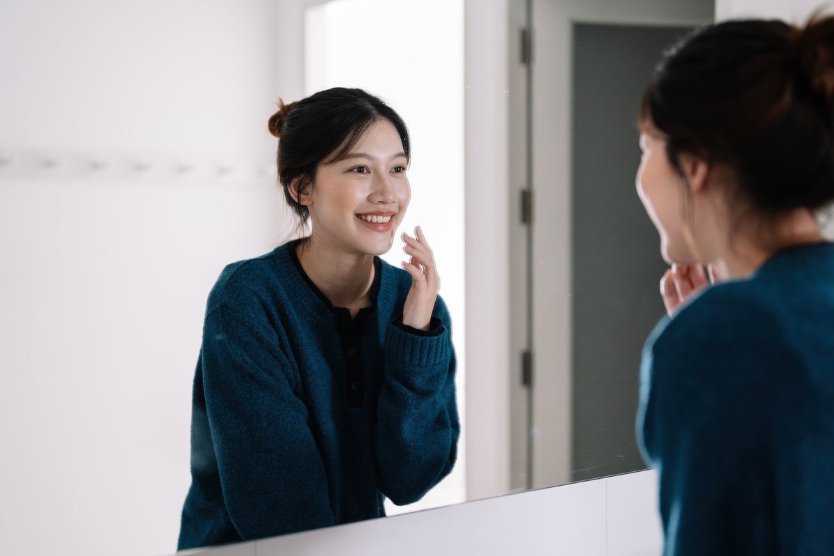 Smiling woman looking at her face in the mirror.