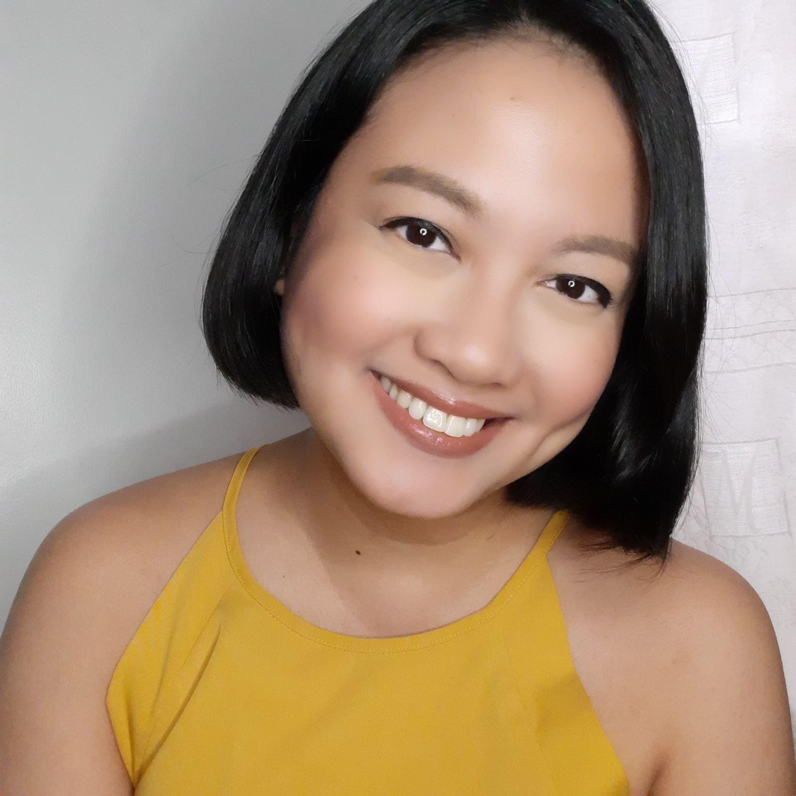 An Asian woman in a yellow tank top smiling at the camera 