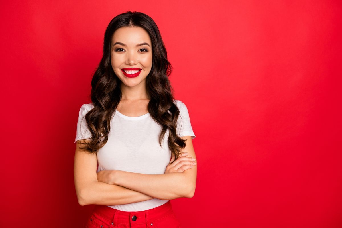 Smiling Asian woman with wavy hair against a red background.