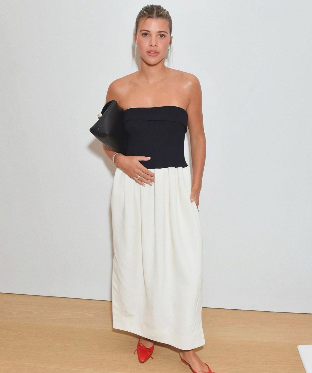 Woman in a black tube top, white skirt, and red shoes.