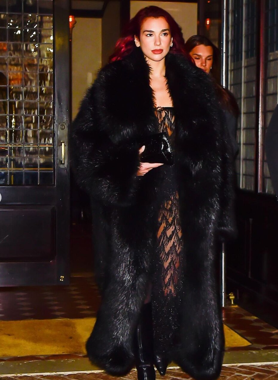 Woman wearing a black furry coat, a sheer dress, and boots.