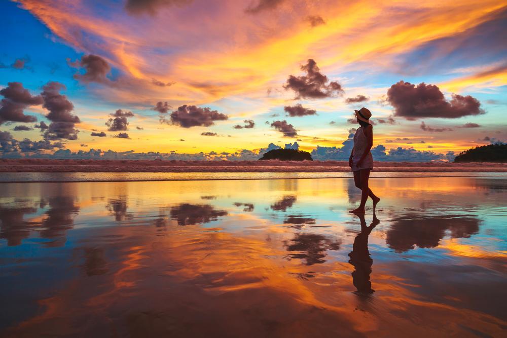 Asian woman walking on beach during golden hour.