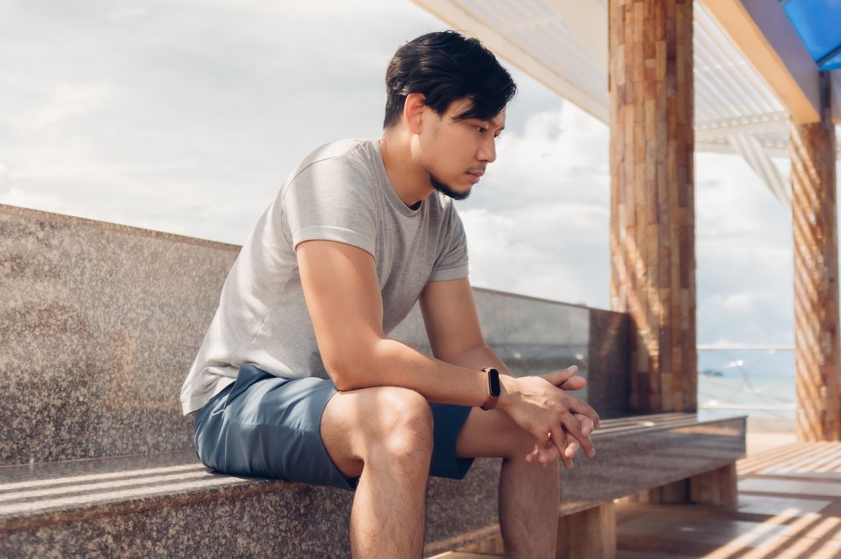 Asian man sitting on bench, contemplating