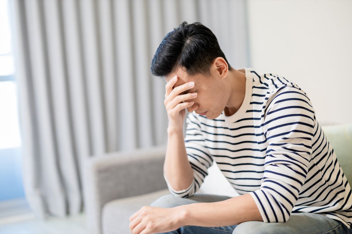 Asian man wearing stripes holding head and looking down 