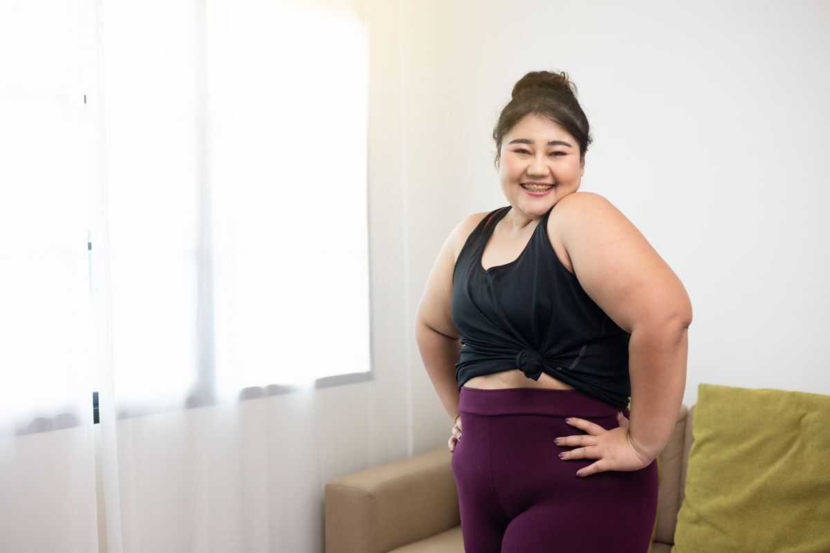 Smiling plus size Asian woman in shaping leggings and a black tank top.
