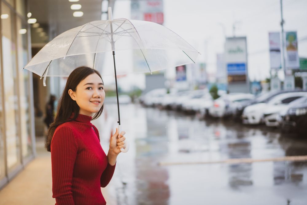 Asian woman in a red top holding a transparent umbrella.