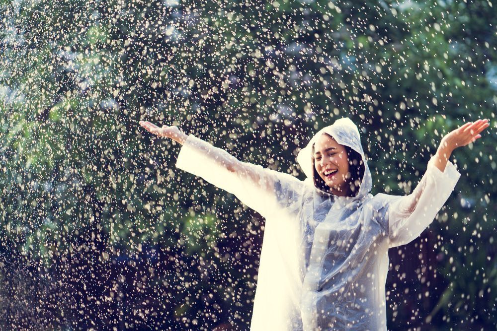 Asian woman wearing a raincoat, dancing in the rain.