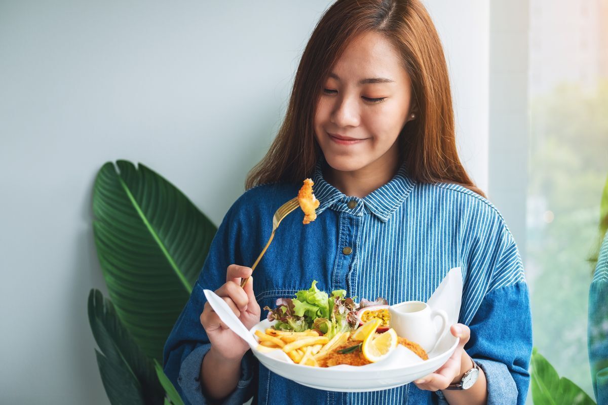 Asian woman in a blue shirt eating salad and fish