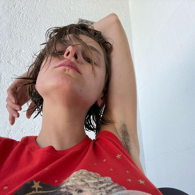 Emma Corrin in a red T-shirt showing her armpit hair.