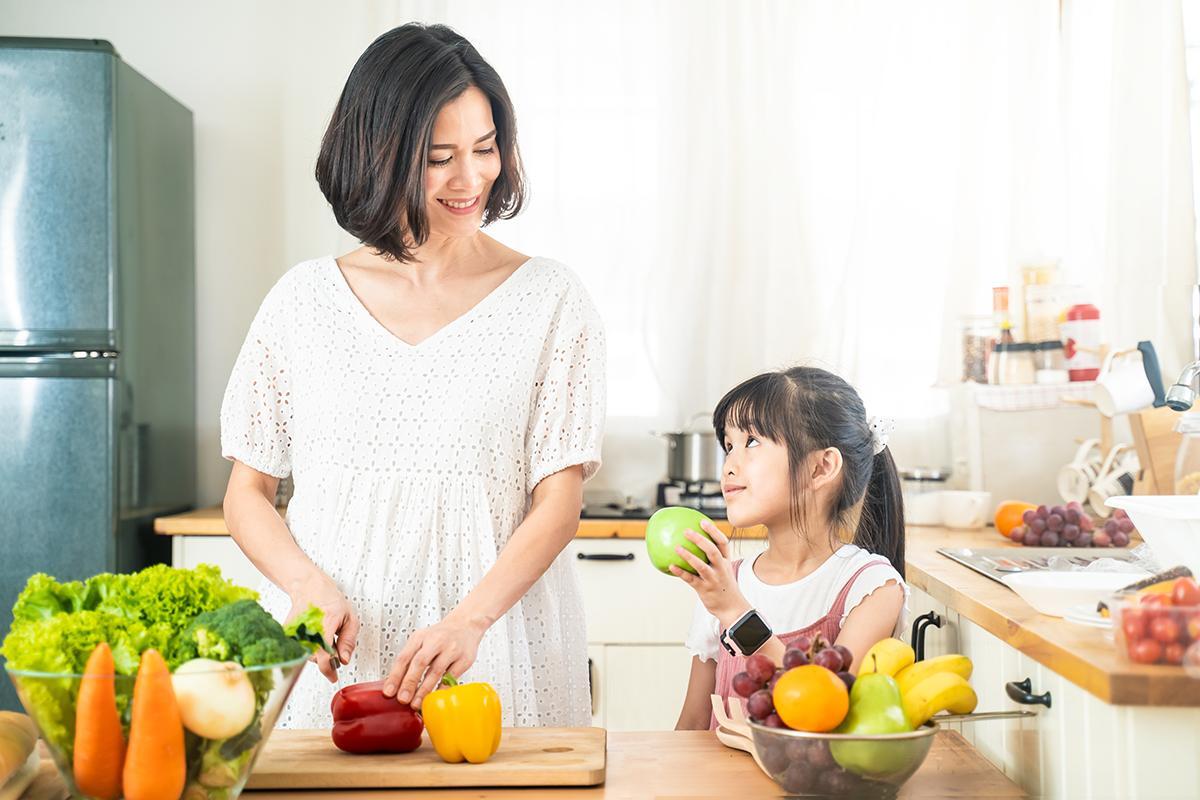 Asian mom and daughter chopping vegetables in kitchen