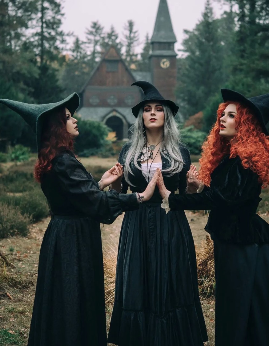 Three women dressed up as witches in long black dresses and black pointed hats