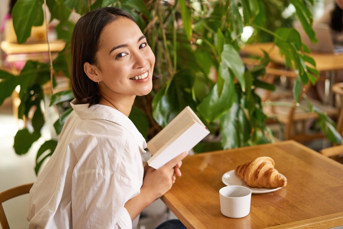 Young woman with a book, sitting in a café with a coffee and croissant on her table