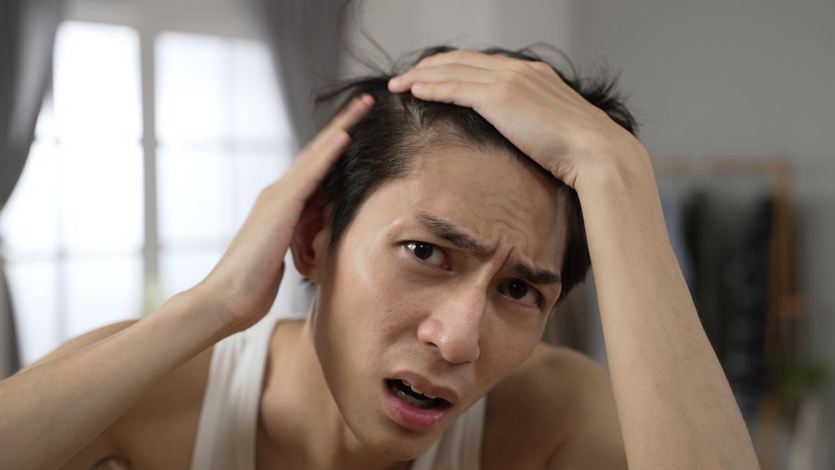 Asian man looking worried while touching his scalp.