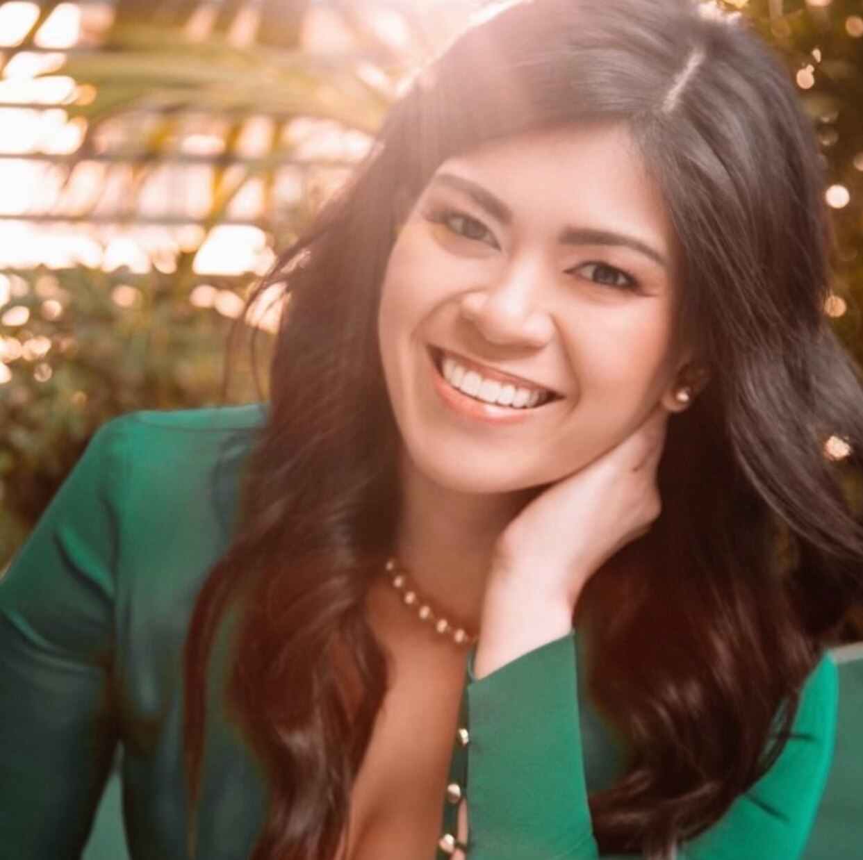 Portrait of an Asian woman with wavy hair smiling and resting her head on her hands.