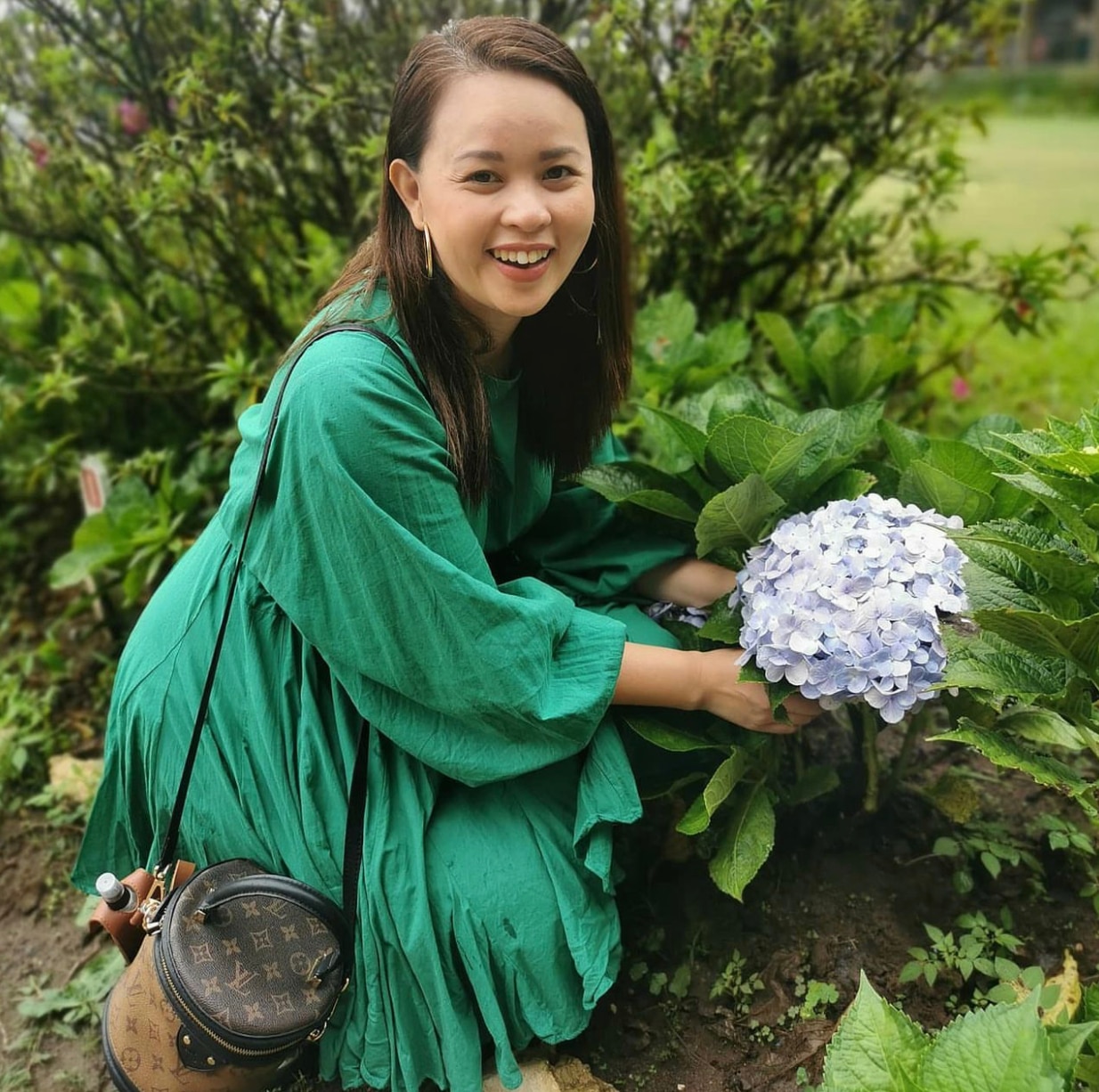 Asian woman wearing green smiling and picking flowers in a garden.