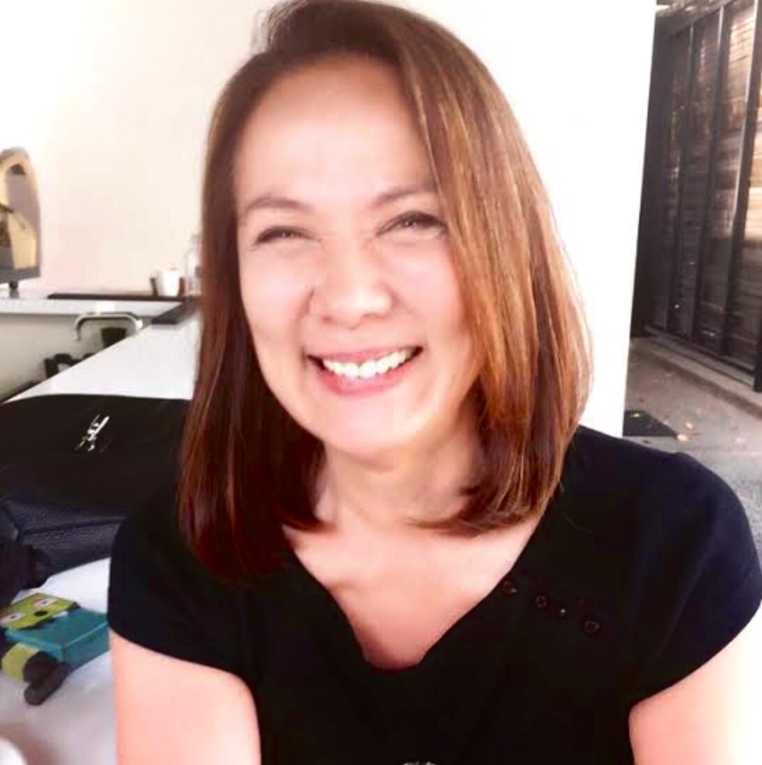 Middle aged Asian woman with straight shoulder length hair smiling.