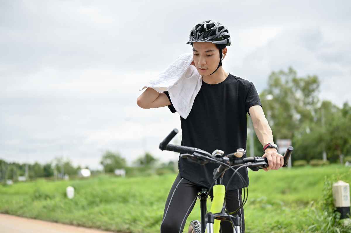 A young man wipes the sweat on his neck while riding his bike.