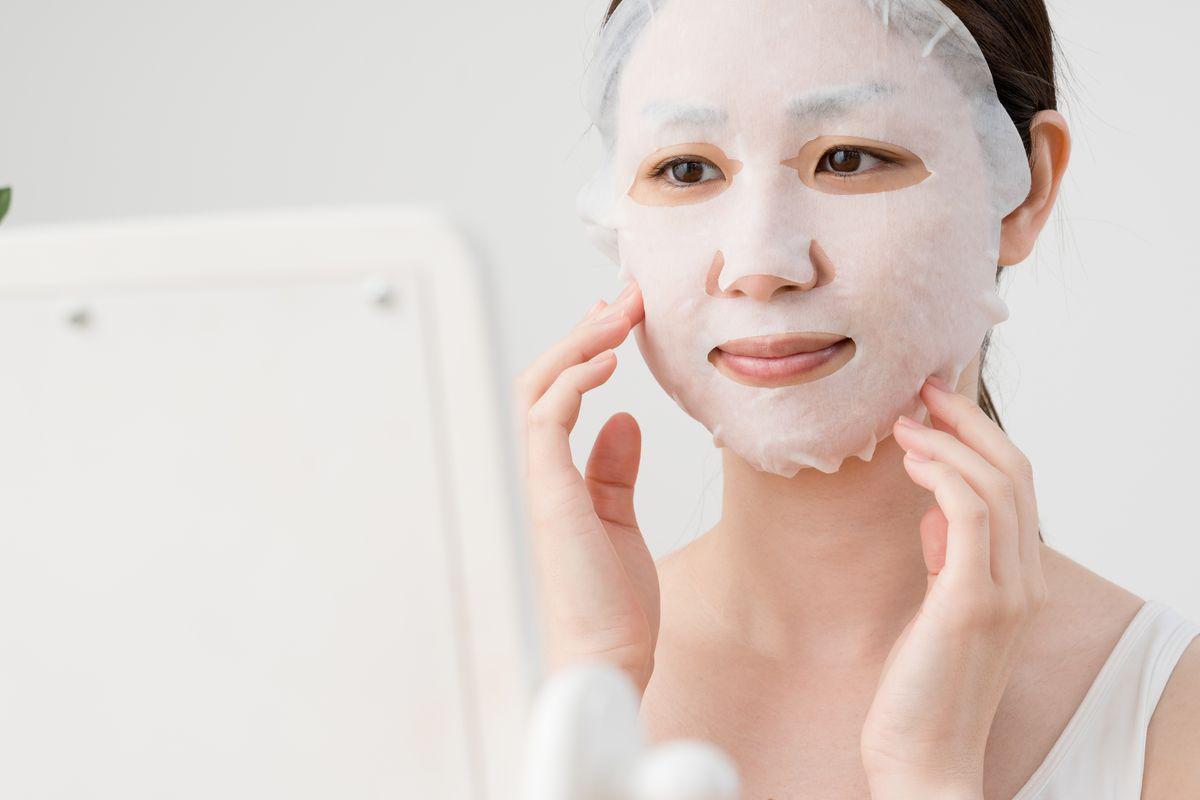 Woman wearing a sheet mask in front of a mirror 