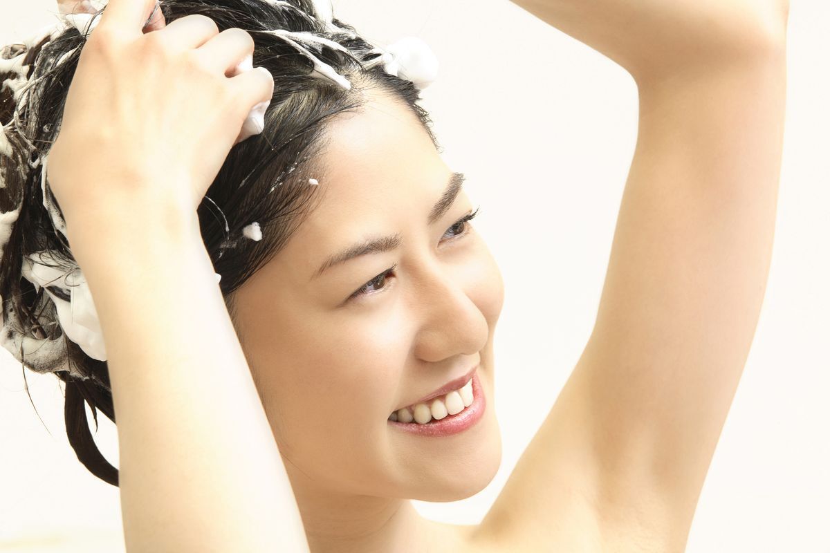 Smiling woman washing her hair with shampoo in the shower.