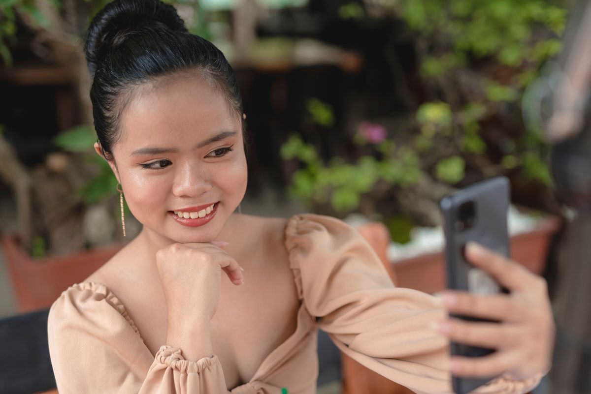 Asian woman in a top knot hairdo taking a selfie.
