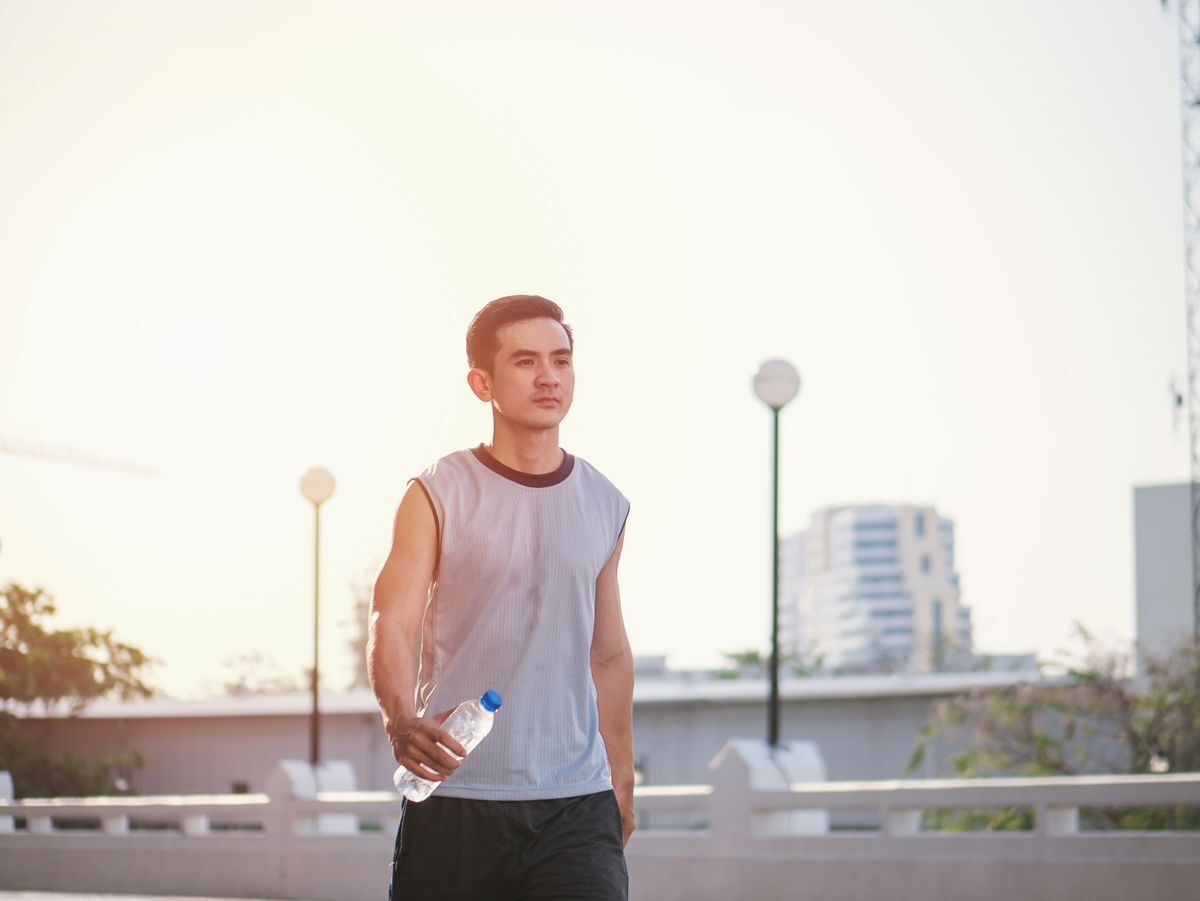 Asian man walking under the sun with bottled water.