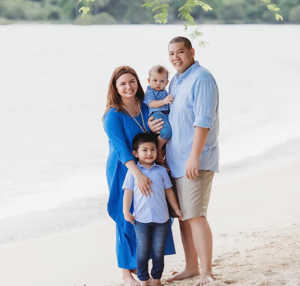 Happy Asian family wearing blue and smiling by the beach.