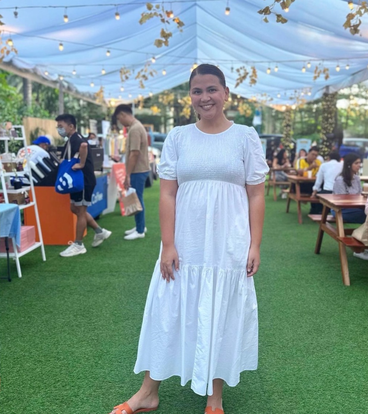 Asian woman wearing a white dress smiling in an outdoor market.