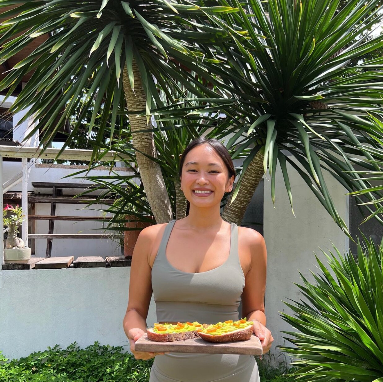 Asian woman smiling and holding a wooden board with avocado toast. 