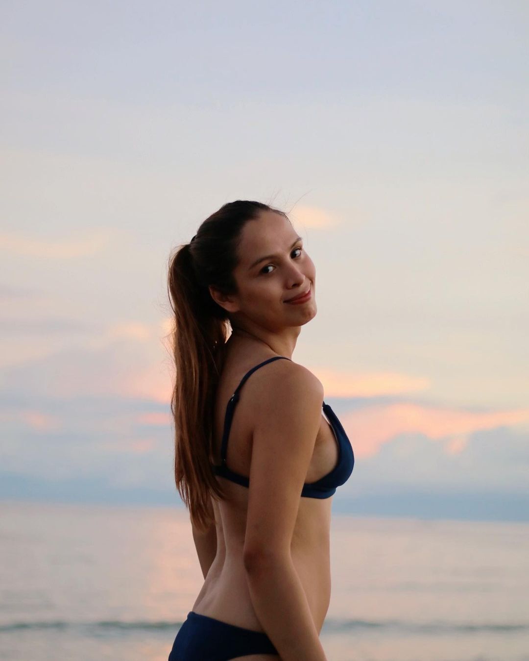 A trans woman smiling at the camera while wearing a bikini at the beach