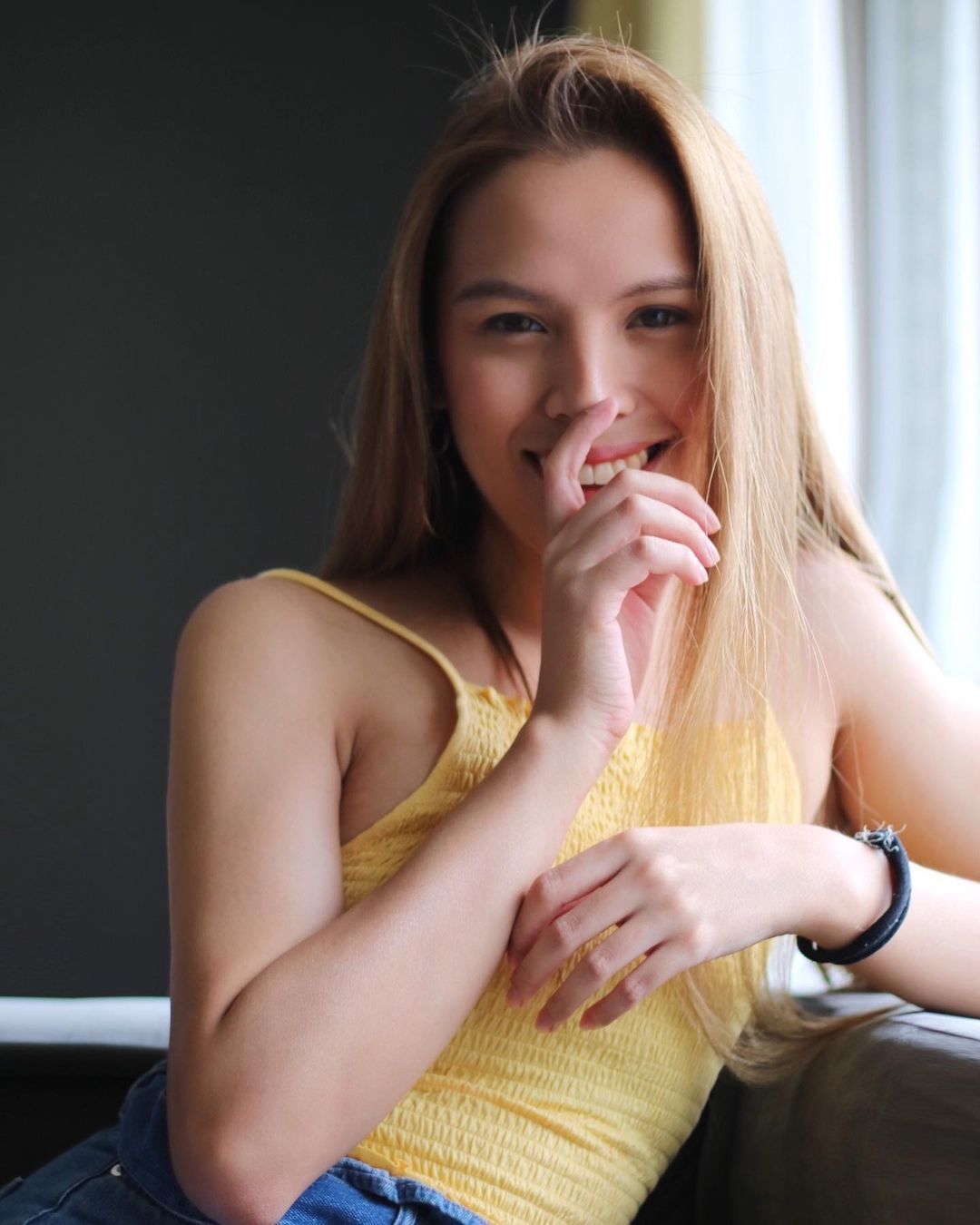 A trans woman wearing yellow with her fingers on her face