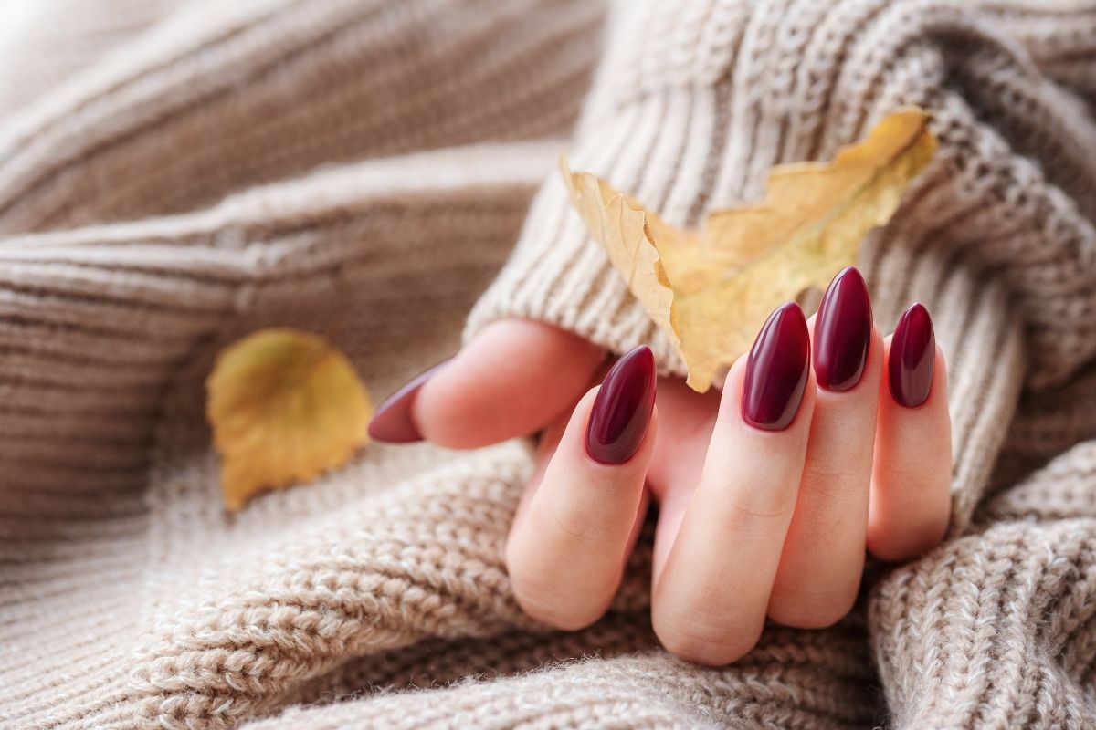 nail màu đỏ mận bàn tay móng màu đỏ mận có chiếc lá vàng trên nền áo len màu be