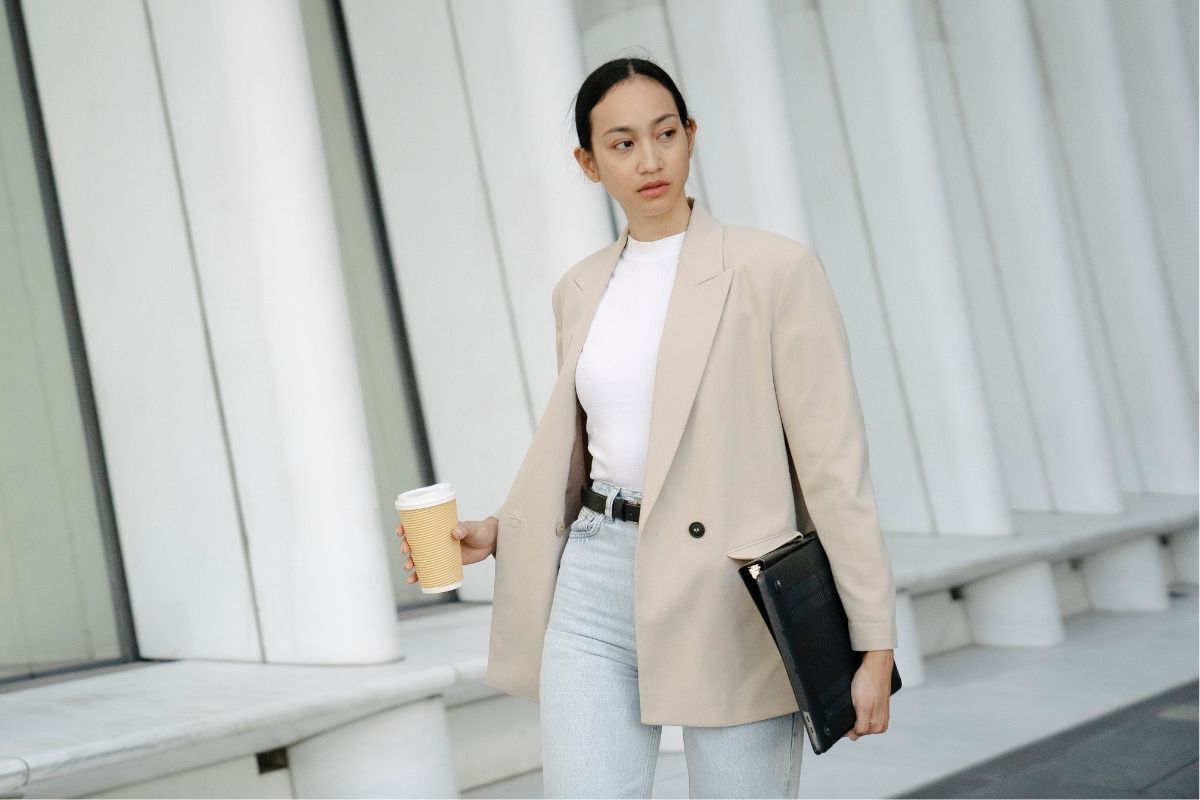 Thời trang sân bay cô gái mặc áo blazer màu be phối quần jeans tay cầm ly nước và tập tài liệu màu đen