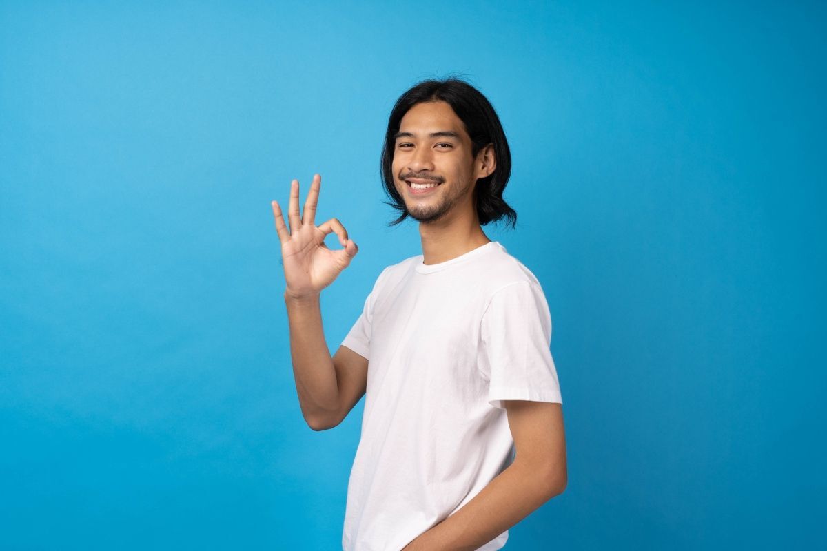 kiểu tóc dài nam đẹp nhất chàng trai mặc áo trắng cười tươi trên nền xanh 