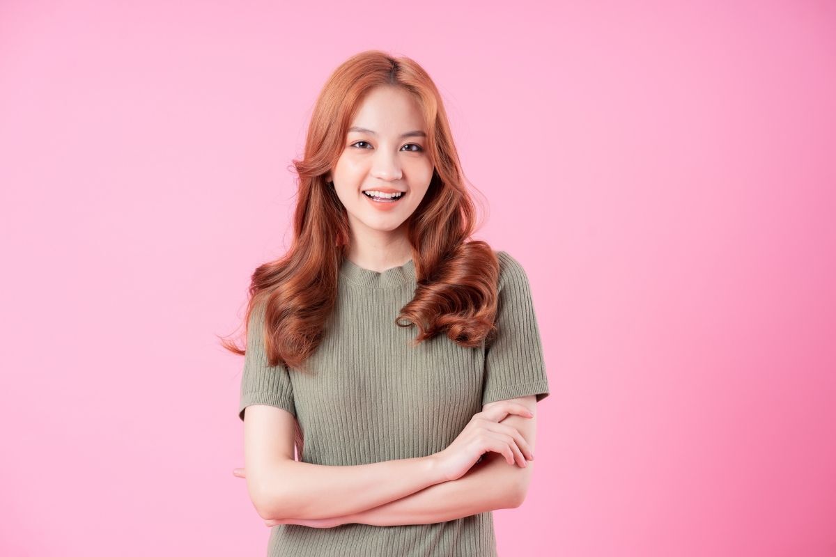 màu tóc cho học sinh đẹp cô gái tóc uốn màu đỏ đâu đồng cười tươi trên nền hồng