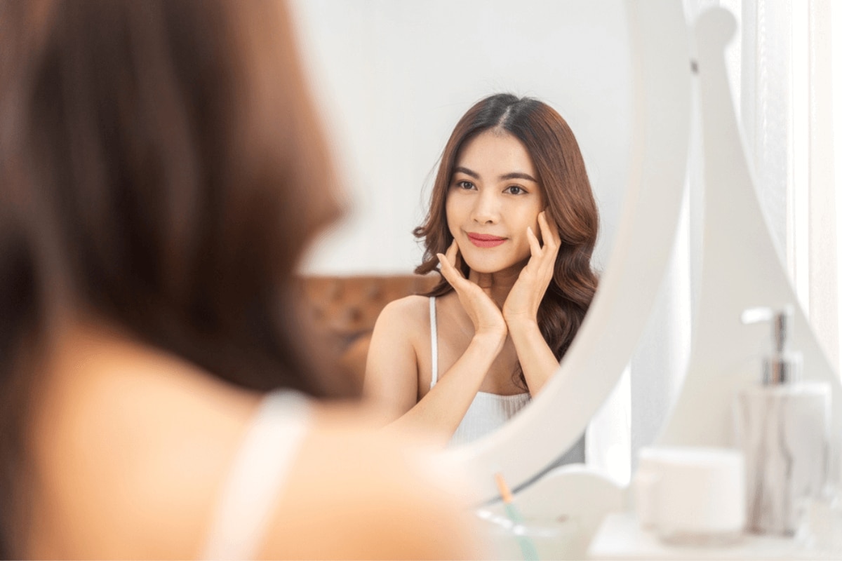 mỹ phẩm thuần chay là gì mỹ phẩm thuần chay bao lâu mới thấy hiệu quả nụ cười của người phụ nữ trẻ xinh đẹp châu Á, làn da trắng khỏe tươi tắn nhìn vào gương