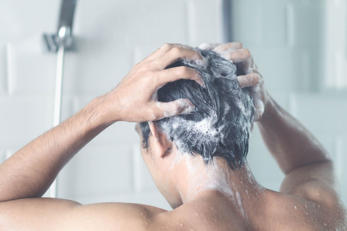 dầu gội trị gàu chàng trai quay lưng đang gội đầu dưới vòi hoa sen