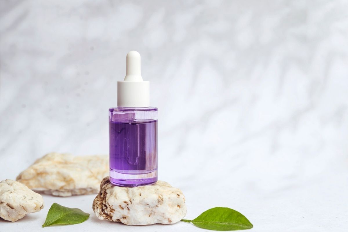 Bakuchiol hỏi nhanh đáp gọn về Bakuchiol chai serum màu tím đặt trên hòn đá cuội