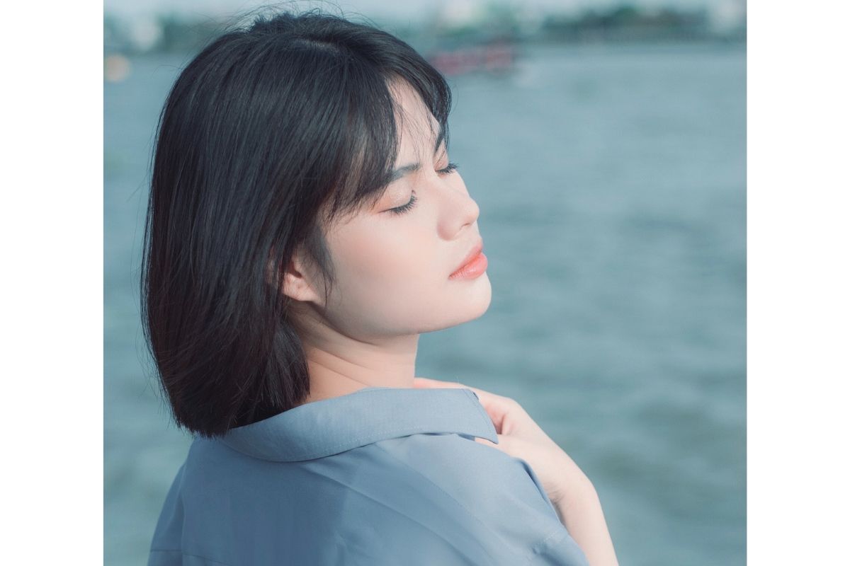 8 kiểu tóc ngắn dễ thương đúng chuẩn kawaii nhật bản cô gái mặc áo sơ mi xanh dương đang nhắm mắt đứng bên bờ hồ