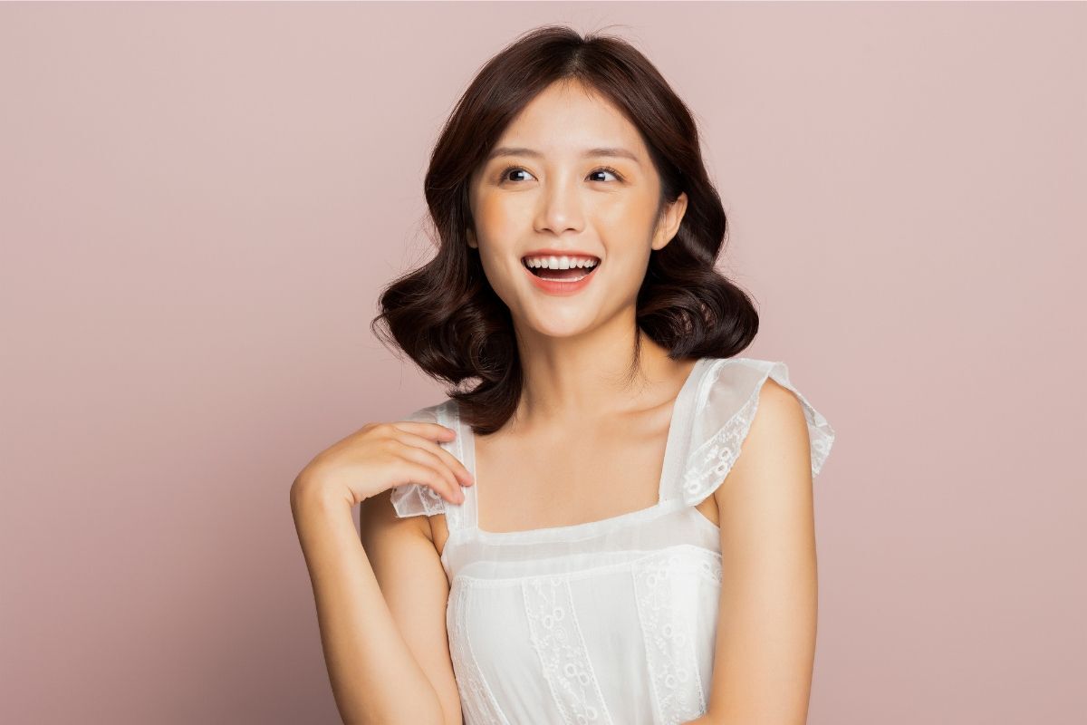 Kiểu tóc ngắn cho mặt dài trán cao cô gái mặc áo cổ vuông màu trắng chụp trên nền tường hồng