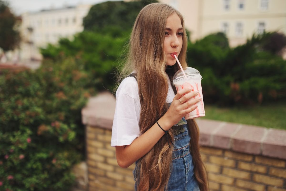 tóc xoăn dài cô gái  mặc váy jean đang cầm ly trà sữa để uống giữa khu vườn xanh