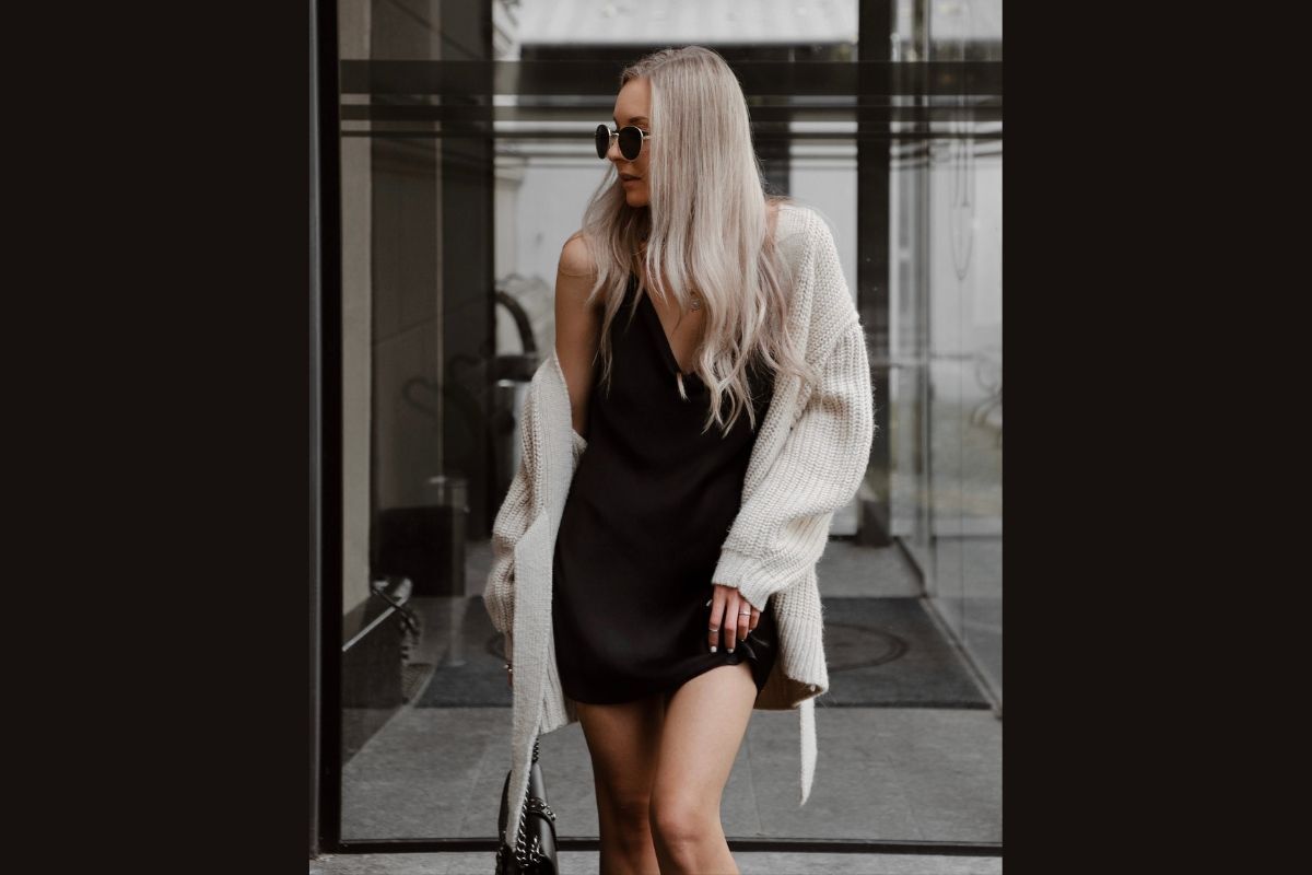 Cô gái đeo kính râm tròn mặc váy liền màu đen phối đồ với áo cardigan màu trắng