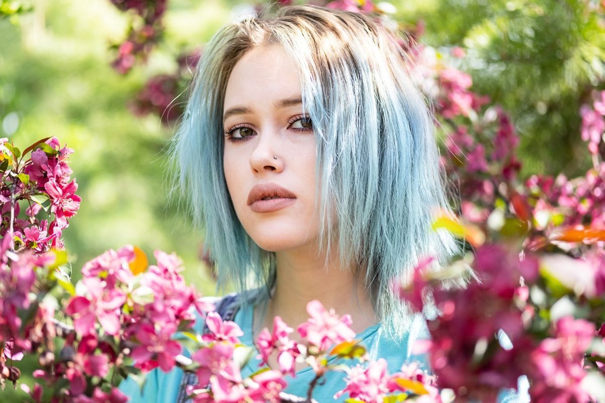 Nhuộm tóc màu xanh khói cô gái đứng giữa những bông hoa màu hồng