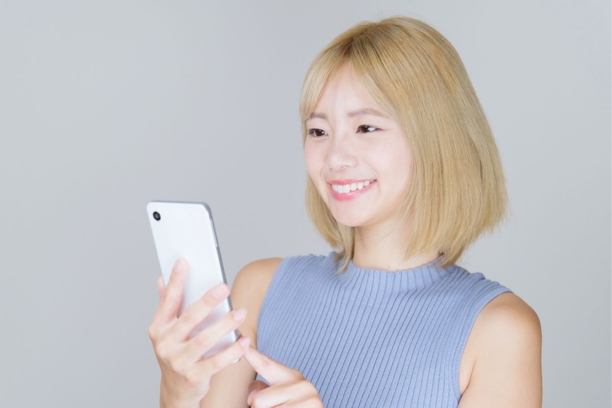 Màu tóc vàng tây cô gái cầm điện thoại màu trắng chụp trên nền xám