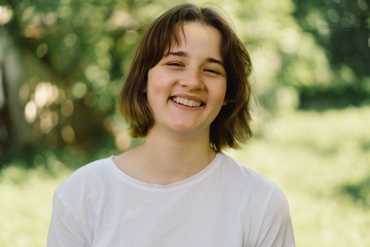 Tóc bob layer cô gái cười tươi đang đứng giữa khu vườn màu xanh lá