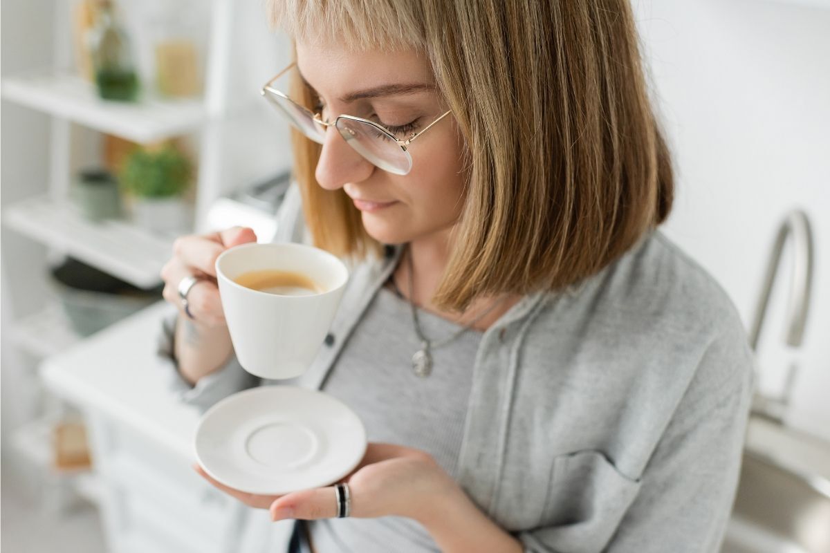 tóc ngắn uốn cụp cô gái đeo kính đang uống cà phê trong căn phòng màu trắng