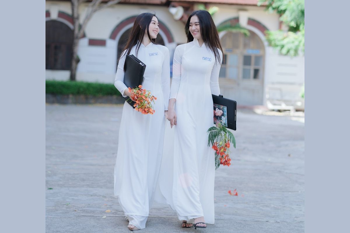 Hai cô gái mặc áo dài trắng đang nắm tay nhau và tạo dáng chụp ảnh áo dài kỉ yếu