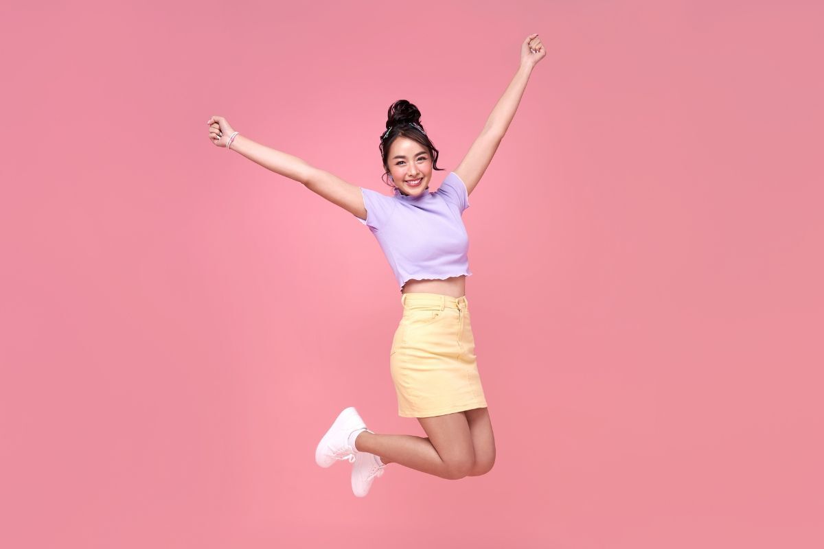 cách phối đồ đẹp cho nữ đi chơi cô gái búi tóc cao bật nhảy trên nền hồng