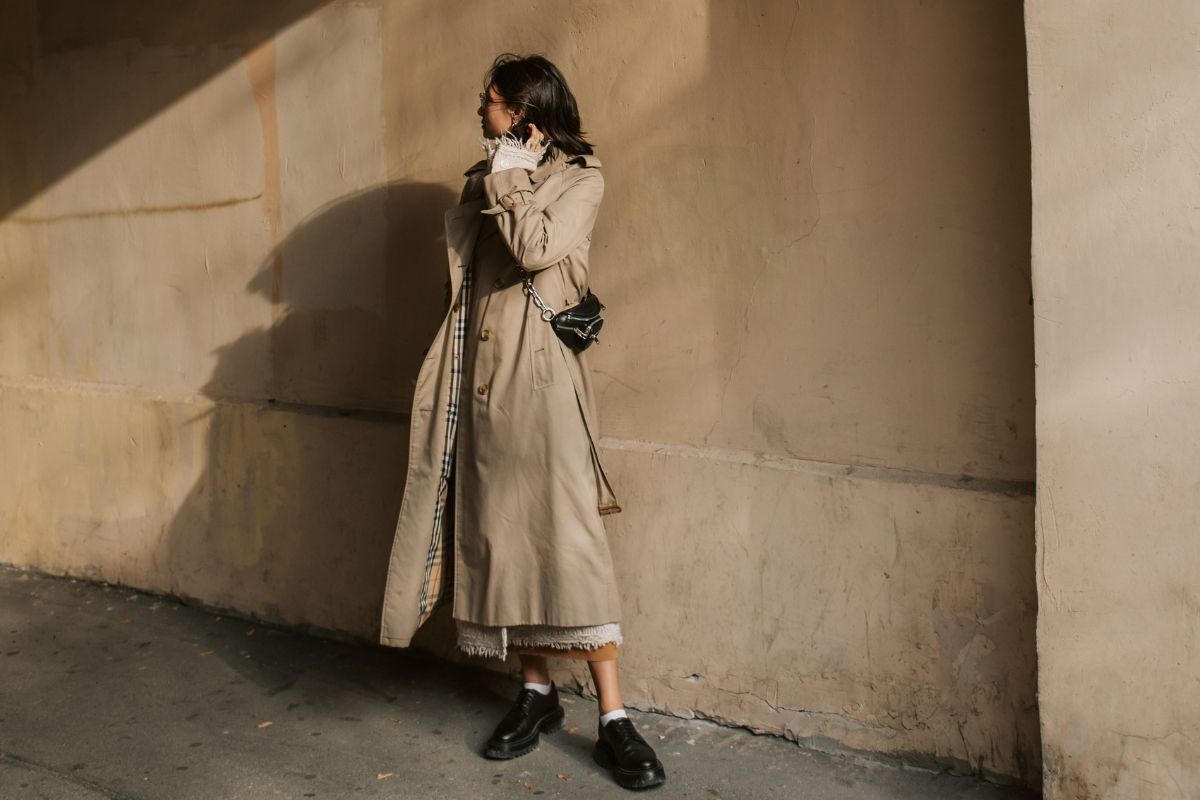 Cô gái mặc áo khoác dáng dài màu be đeo túi xách nhỏ màu đen 
