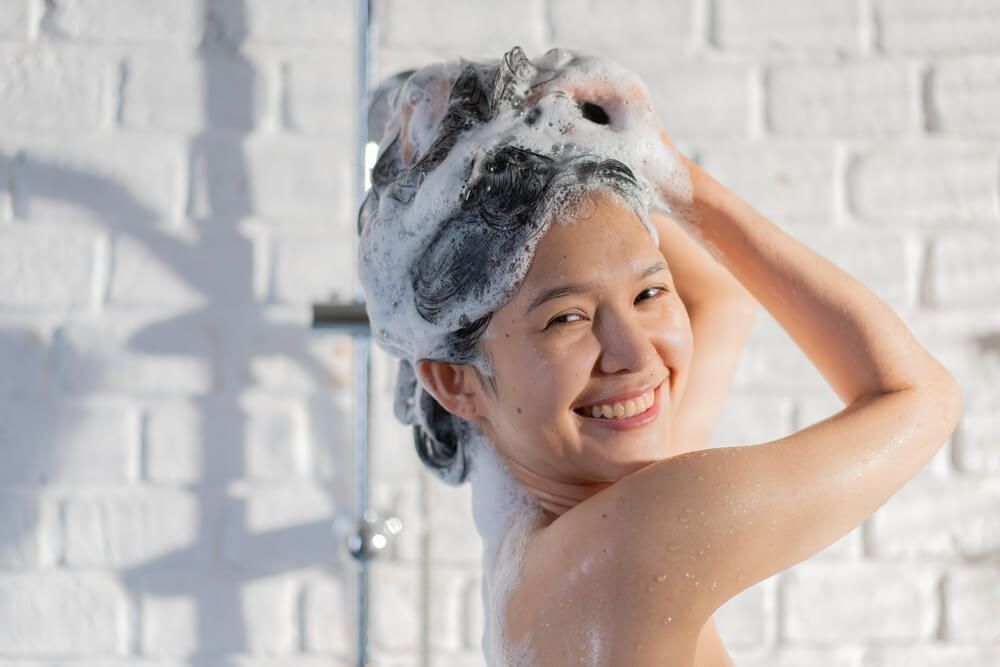 tóc sâu cô gái đang cười tươi và gội đầu dưới vòi hoa sen